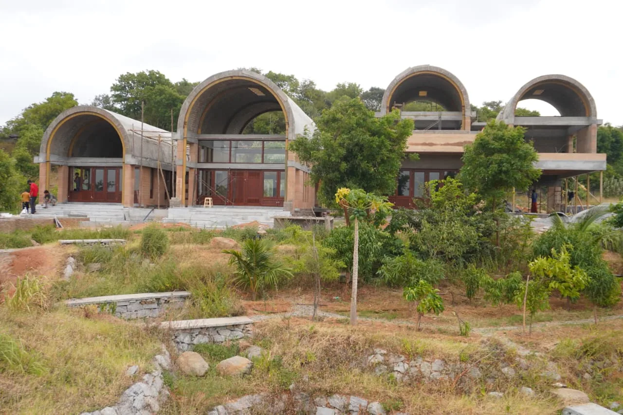 A contemporary building in exposed local brick with bamboo-patterned windows, set in a dry Deccan landscape.